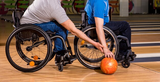 Two young disabled men in wheelchairs playing bowling in the club