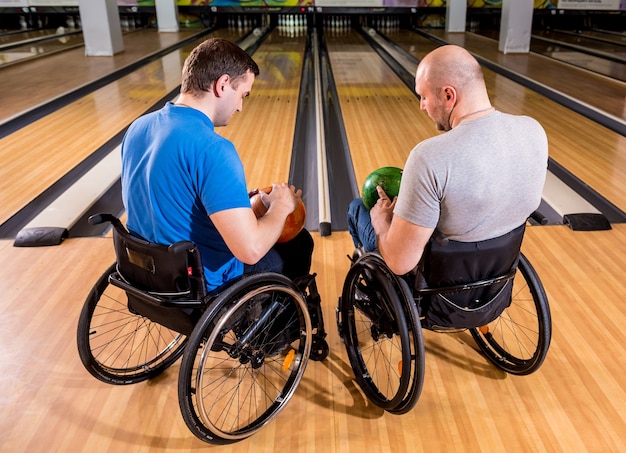 Photo two young disabled men in wheelchairs playing bowling in the club