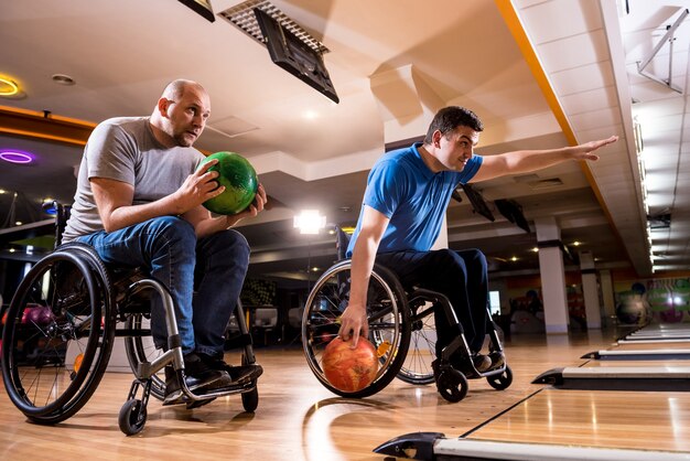 Two young disabled men in wheelchairs playing bowling in the club