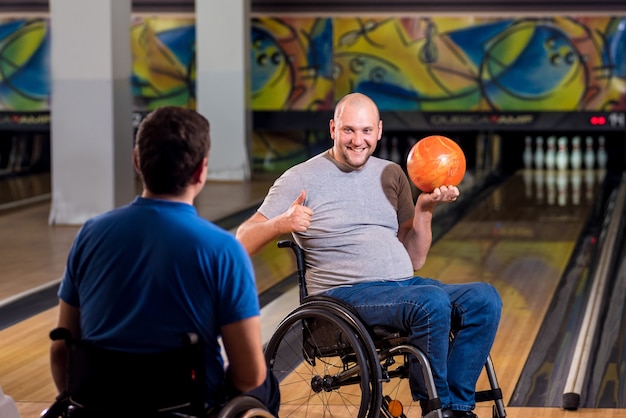 Two young disabled men in wheelchairs playing bowling in the club