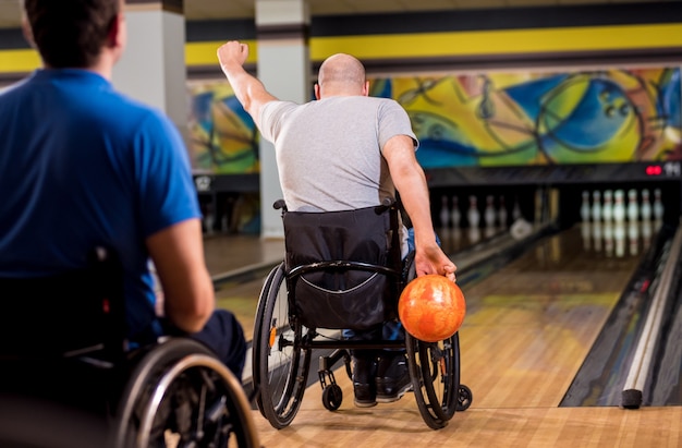 Two young disabled men in wheelchairs playing bowling in the club