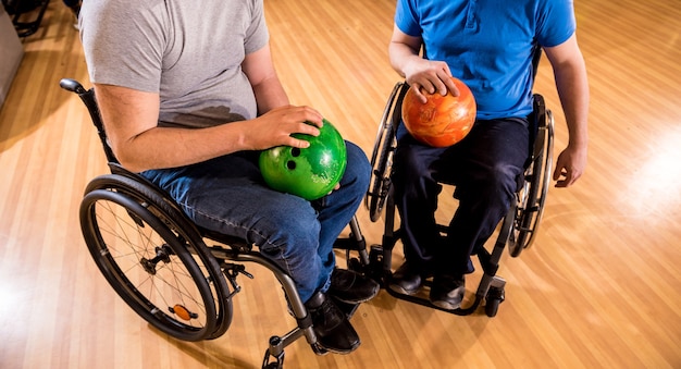 Photo two young disabled men in wheelchairs playing bowling in the club