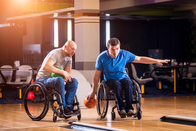 Two young disabled men in wheelchairs playing bowling in the club