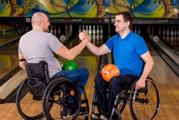 Two young disabled men in wheelchairs playing bowling in the club