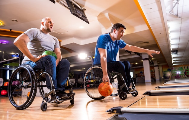 Photo two young disabled men in wheelchairs playing bowling in the club