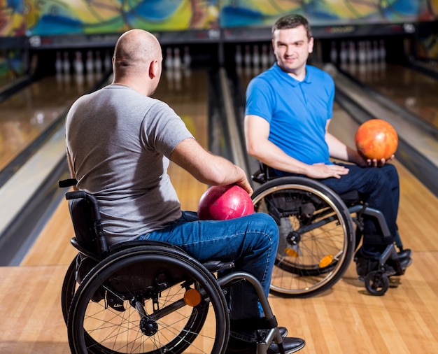 Two young disabled men in wheelchairs playing bowling in the club