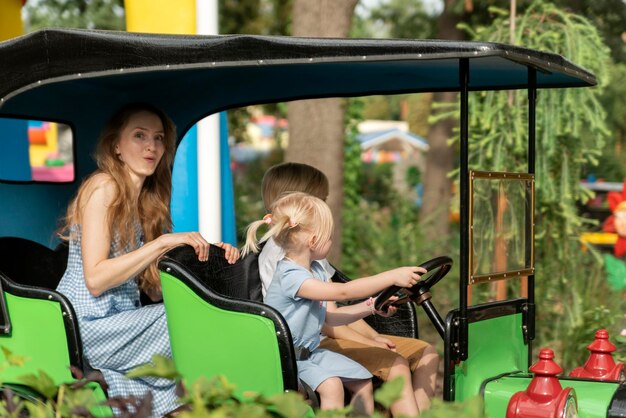 Two young drivers of the child roll their mother in car in an amusement park Nanny looks after the children in theme park