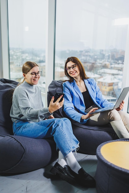 Two young female freelancers working remotely in the lounge area at a laptop The concept of remote work Friendly relations between colleagues