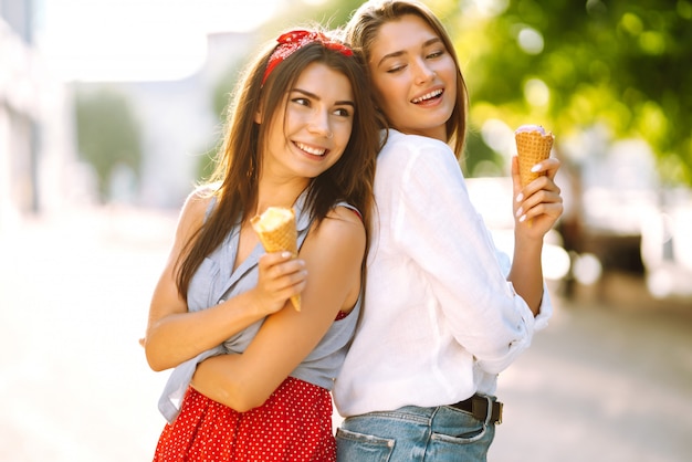 2人の若い女性の友人が楽しんで、アイスクリームを食べています。