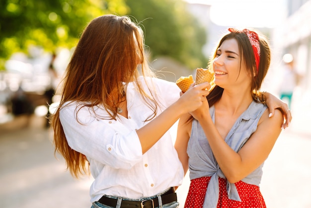 2人の若い女性の友人が楽しんで、アイスクリームを食べています。