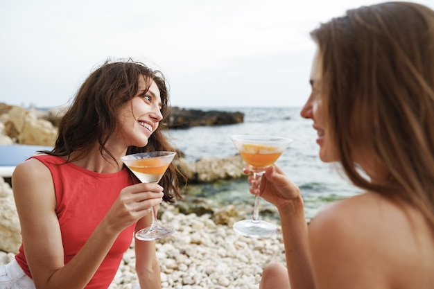 Two young female friends having picnic on a beach drinking cocktails