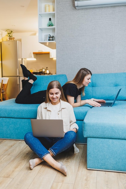 ラップトップでソファに座って自宅で働く 2 人の若い女性の友人 美しい女子学生はラップトップでレポートを書きます