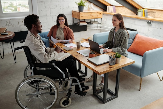 Two young female managers looking at confident male colleague in wheelchair