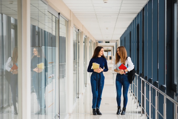 Two young female students standing with books and bags in the hallway