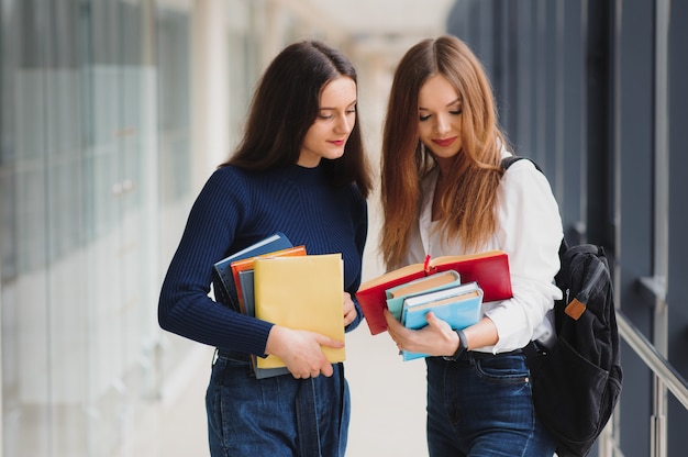 Two young female students standing with books and bags in the hallway