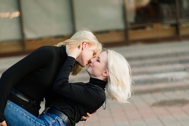 Two young females walking smiling embracing and kissing outdoor in the city