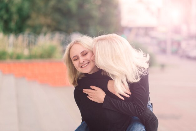 Two young females walking smiling embracing and kissing outdoor in the city