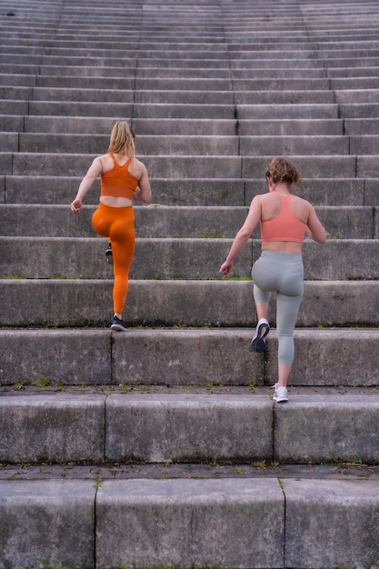Две молодые фитнес-девушки в городском парке бегут по большим ступеням