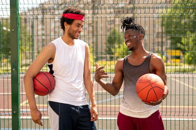 Two young friendly basketball playmates discussing some curious moments of game while standing by fence of playground