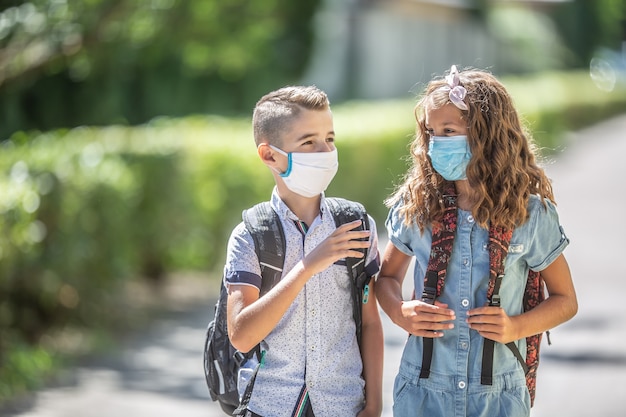 Two young friends classmates with face masks talk on their way to school during the Covid-19 quarantine.