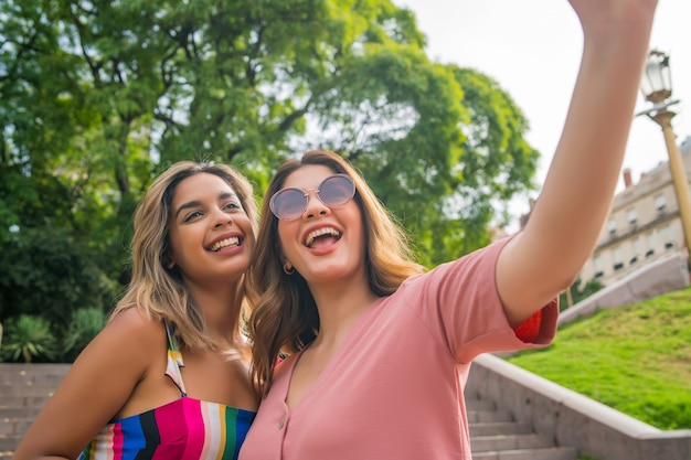 Two young friends taking a selfie and smiling while standing outdoors. Urban concept.