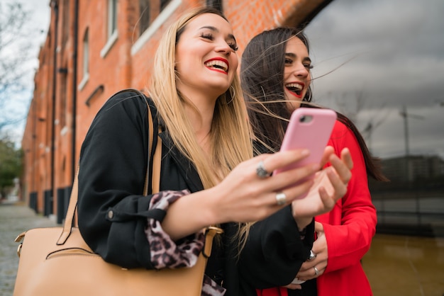 Two young friends using their mobile phone outdoors.