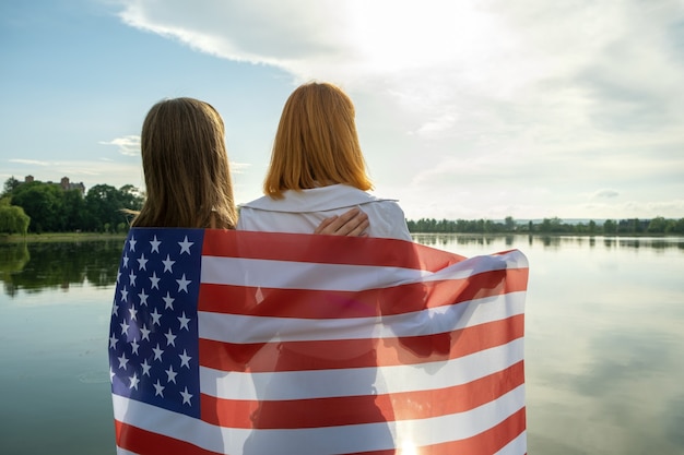 Due giovani amiche donne con bandiera nazionale usa sulle spalle