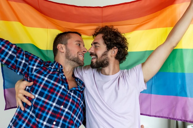 Due giovani amanti gay che si baciano affettuosamente due giovani amanti maschi in piedi insieme contro una bandiera dell'orgoglio affettuosa coppia gay che condivide un momento romantico insieme