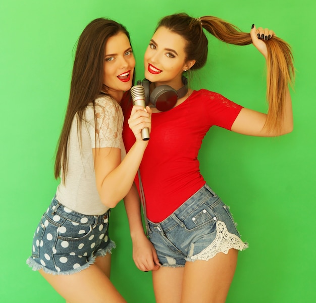 Two young girl friends standing together and having fun over green background