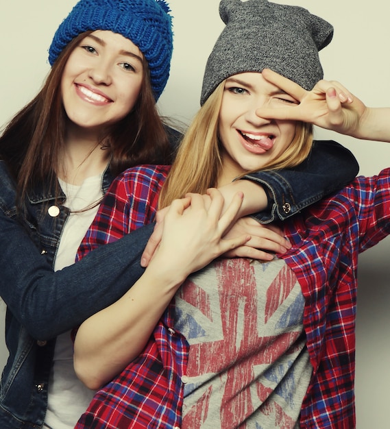 Two young girl friends standing together and having fun. Showing signs with hands. Looking at camera