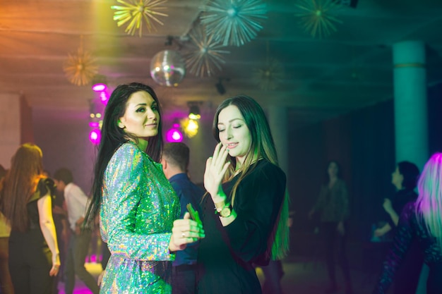 Two young girls in a fashionable dresses are dancing in a nightclub