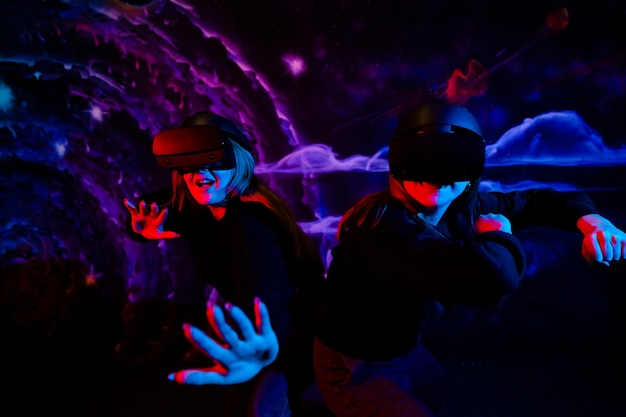 Две молодые девушки сестры подруги в виртуальных очках веселятся в неоновом синем и красном свете, фото высокого качества
