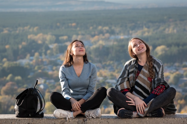 Фото Две молодые девушки сидят на фоне природы и улыбаются. отдых с другом, каникулы. передний план.