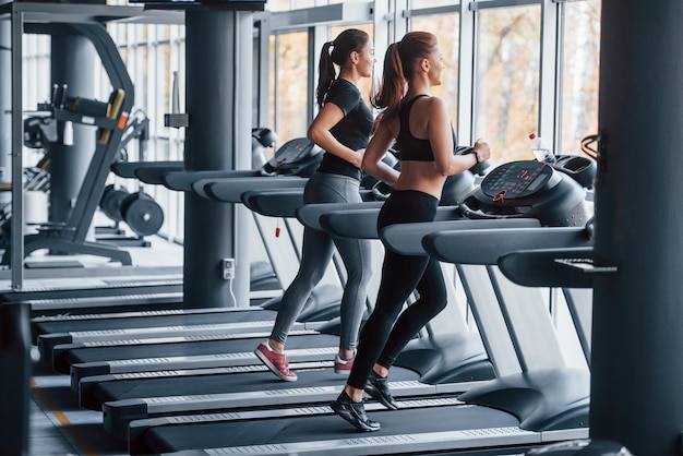 Two young girls in sportive clothes is in the gym together at treadmill.