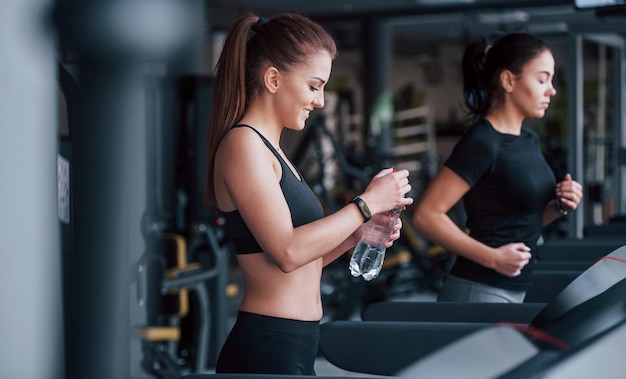 Two young girls in sportive clothes is in the gym together at treadmill.