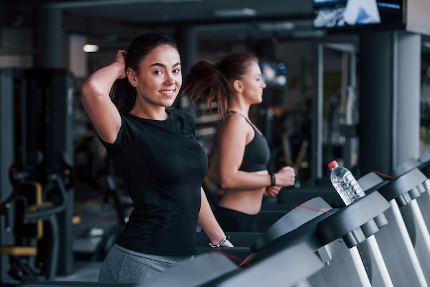 Two young girls in sportive clothes is in the gym together at treadmill.