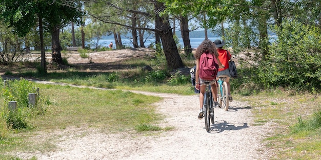 Two young girls teenagers friends on bike ride in Lacanau lake sand beach in web banner template on summer day