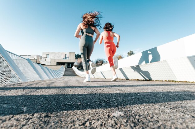 Two young girls training hard running outdoors doing exercise wearing sportswear. Fitness girls working out together. Low angle image moving motion image. African girls sunny day lens flare copy space