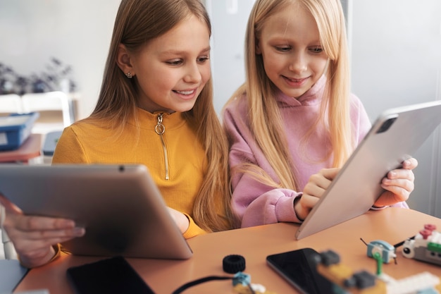 Photo two young girls using tablets and electronic parts to build a drone