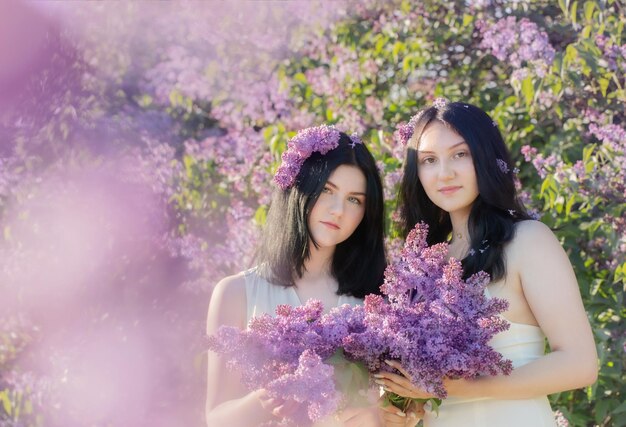 Two young girls with blooming lilac in sunlight