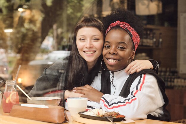 Two young gorgeous girlfriends sitting by served table in embrace