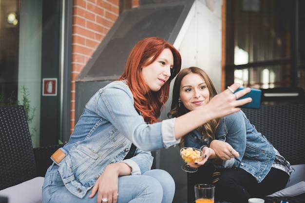 Two young handsome caucasian blonde and redhead straight hair women sitting in a bar