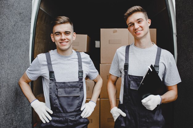 Due giovani lavoratori belli sorridenti che indossano uniformi sono in piedi davanti al furgone pieno di scatole