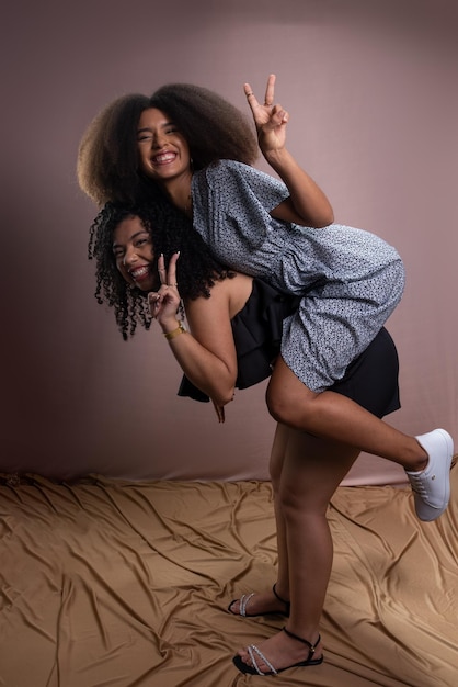 Photo two young happy beautiful friends one carries the other on its back friendship and relaxation concept isolated on salmoncolored background