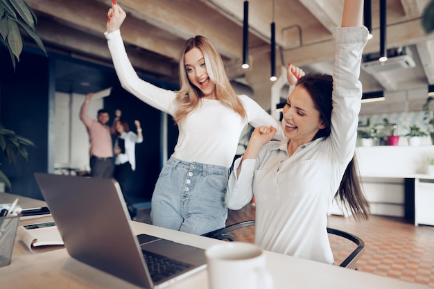 Two young happy businesswomen celebrating project success in office