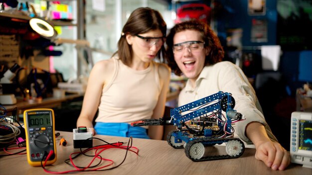 Two young happy engineers fixing a mechanical robot car in the workshop using VR virtual reality