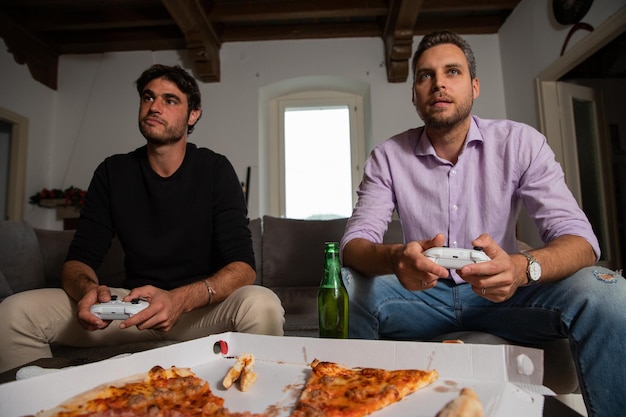 Two young happy friends playing video games while sitting on the couch