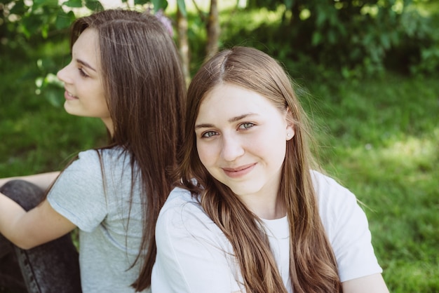 写真 2人の若い幸せな10代の少女が緑の芝生の公園で休んでいます。女性の友情。ソフトセレクティブフォーカス。