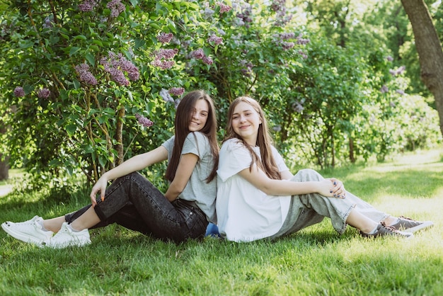 2人の若い幸せな10代の少女が緑の芝生の公園で休んでいます。女性の友情。ソフトセレクティブフォーカス。