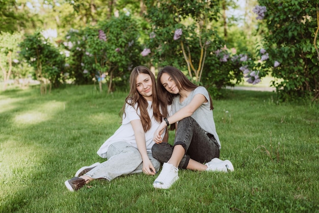 Two young happy teenage girls are resting in the park on the green grass. Female friendship. Soft selective focus.